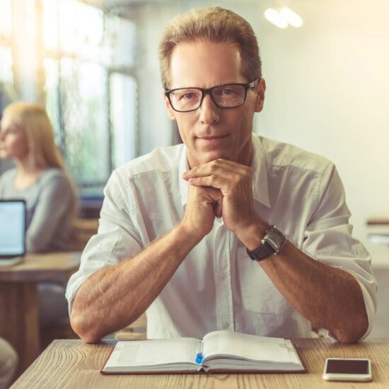 Businessman in shirt and eyeglasses is looking at camera.